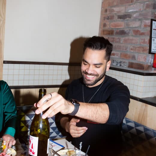 A guest smiling as he opens a bottle of wine